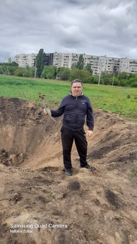 A member of our team Yevgen Tytarenko holds the part of a rocket he found in a crater near the Horizon residential district seen behind his back.